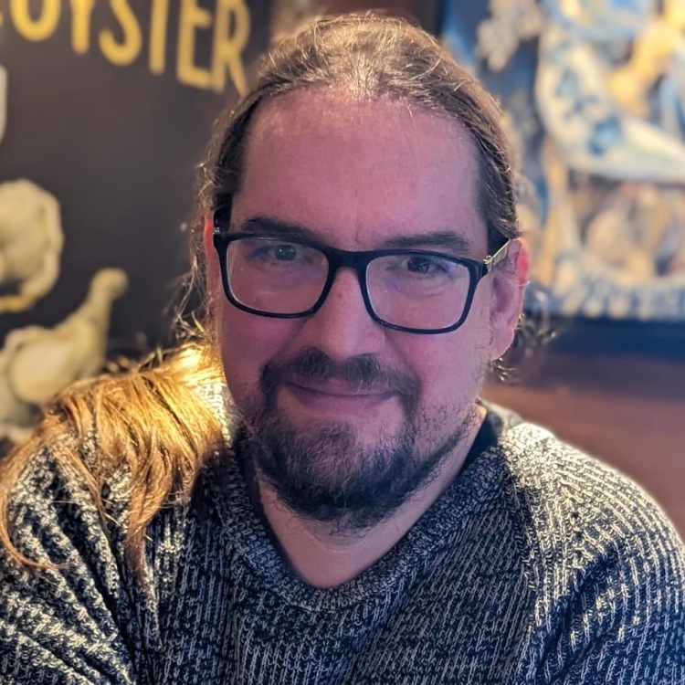 Rob Clarke. Rob has long brown hair in a ponytail and dark-rimmed glasses. He's wearing a woolly jumper.