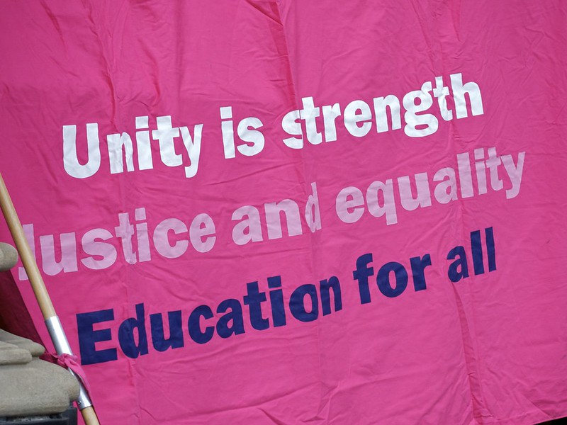 Bright pink banner with the slogan "Unity is strength, Justice and equality, Education for all'